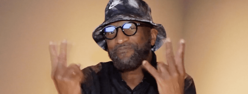 Man wearing hat and glasses, gesturing peace sign.